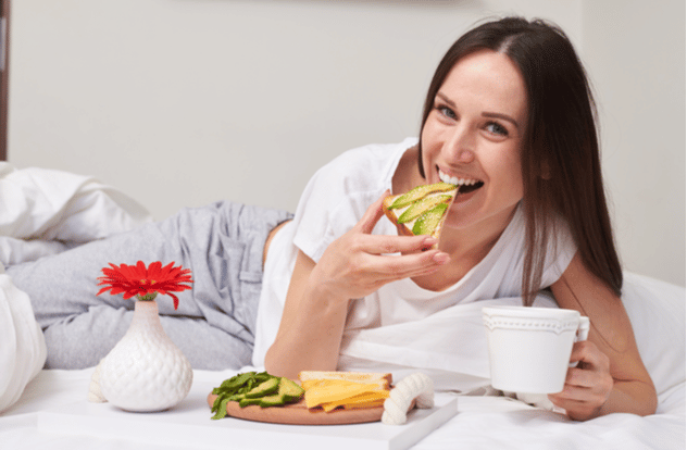 brunette tasting sandwich with avocado and savoring aromatic tea