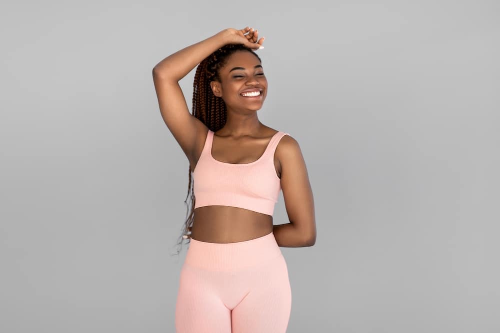 Portrait of happy young black woman in sports outfit posing and smiling on grey studio background. Fit millennial African American female being in great shape, leading active lifestyle
