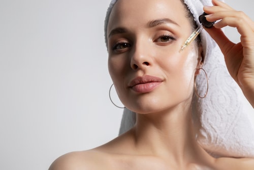 woman in bath towel on head isolated on copy space applying oil serum