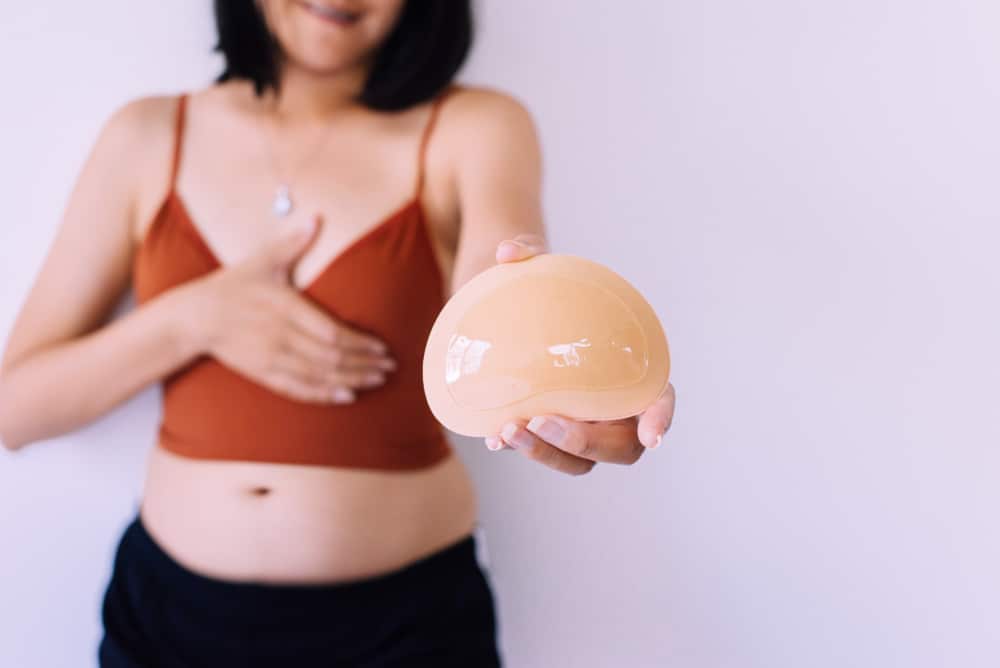 Woman holding a breast implant, considering breast augmentation after pregnancy.