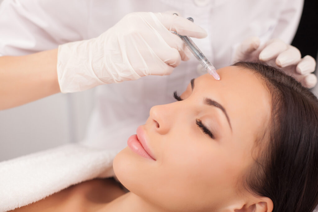 Close up of hands of expert beautician injecting botox in female forehead