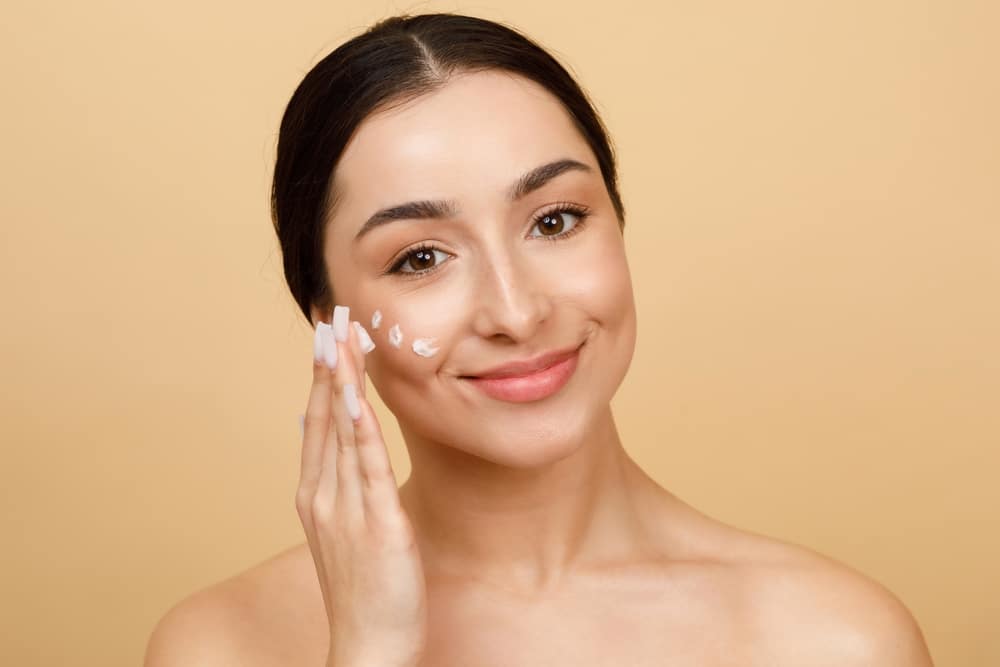 Woman with glowing skin applying medical grade skincare products.