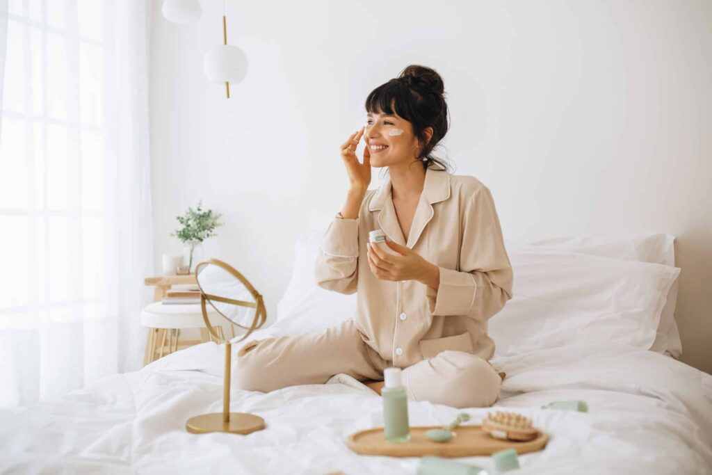 Woman applying anti-aging skin care products while sitting in bed
