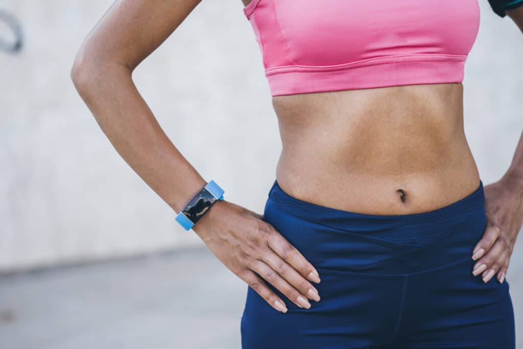 Woman in workout clothes showing a toned abdomen, illustrating core strength and abdominal muscle toning for CoolTone treatment.